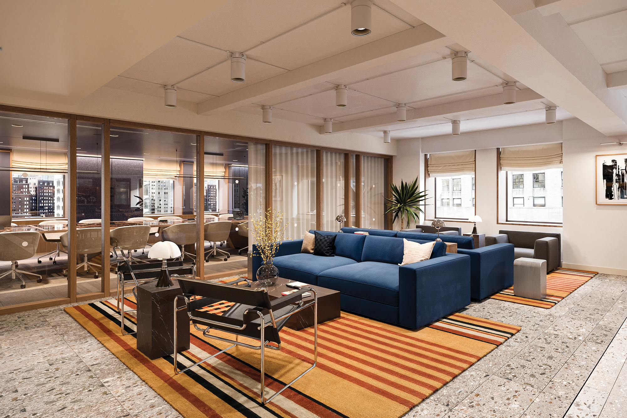 A communal sitting area with blue, gray and black furniture on a colorful orange carpet sits alongside the glass-lined boardroom.