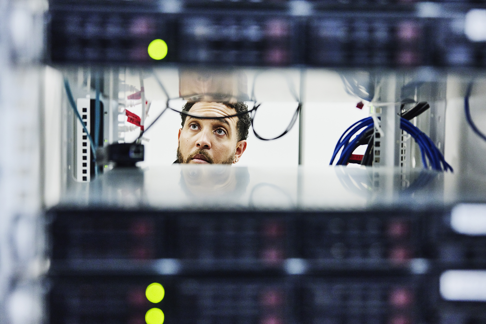 A photo looking through server rack of male IT professional working in data center.