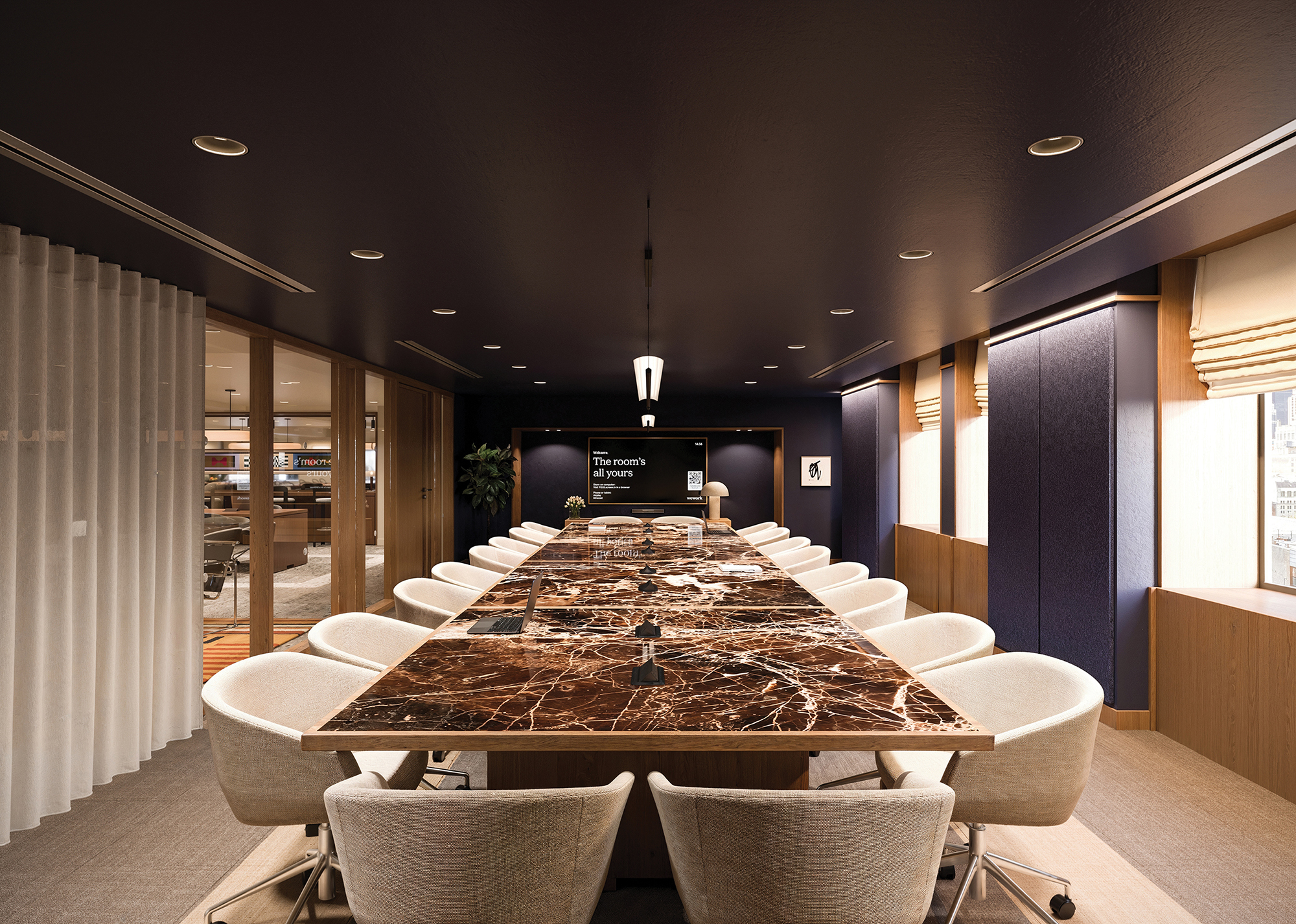 A boardroom includes a dark ceiling, a long, brown table and two rows of white seats.