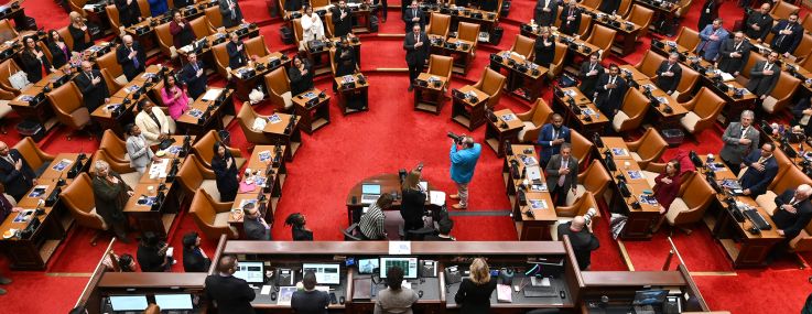 Assembly members stand for the Pledge of Allegiance in the Assembly Chamber in the New York State Capitol.