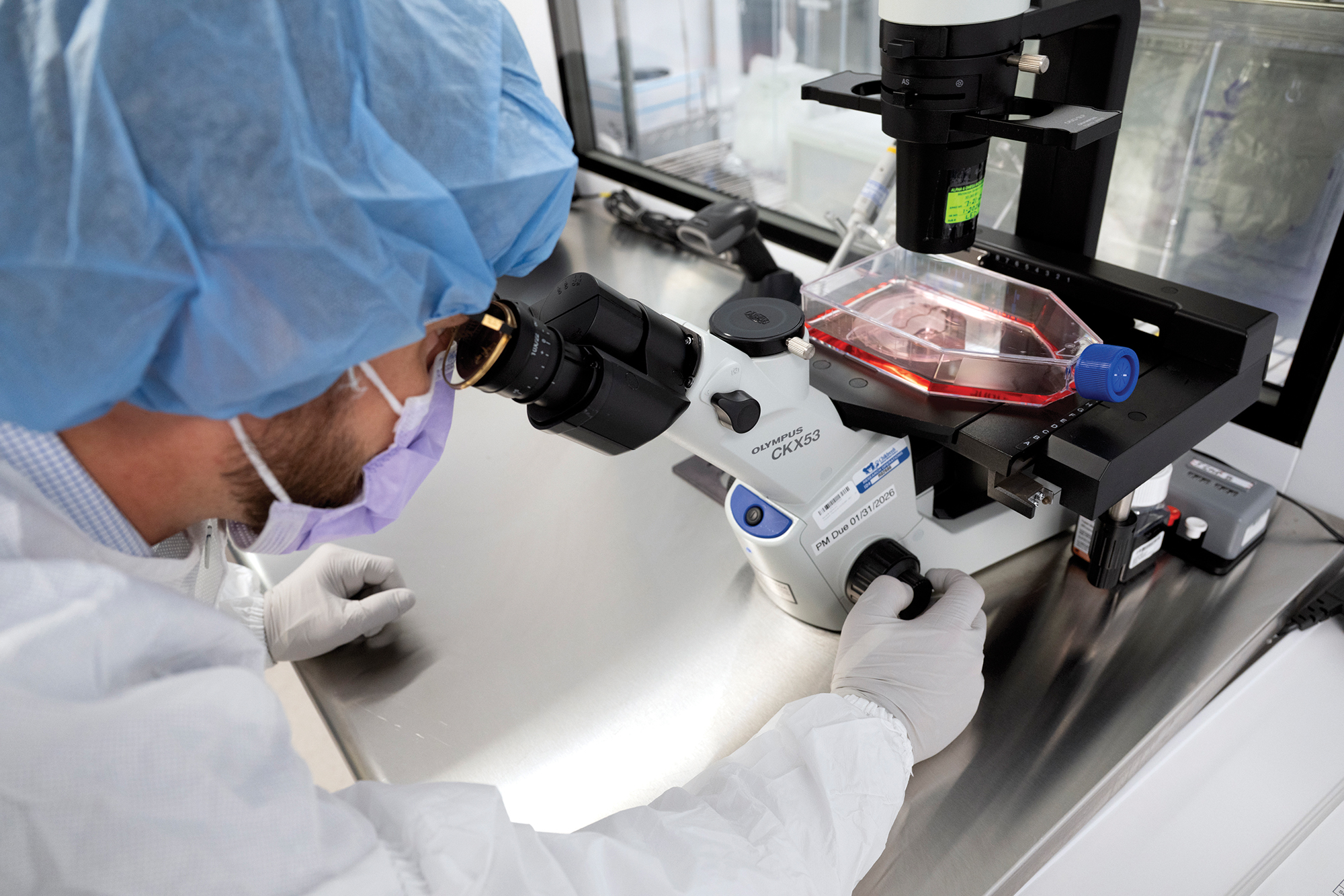 A man in a lab coat looks through a microscope.