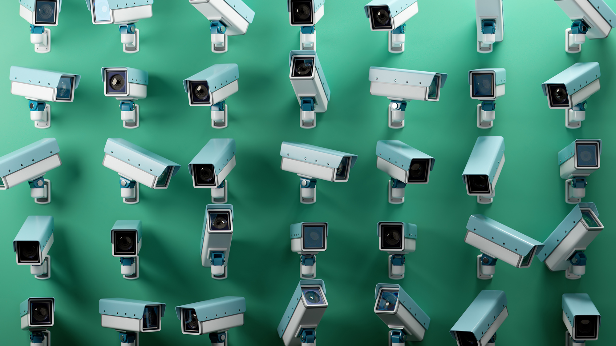 An array of multiple security cameras mounted on a green wall.