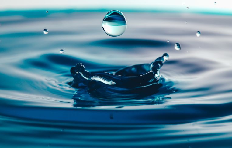 Dark blue water droplets splashed closely on the water surface. It creates a water wave and a perfect crown.