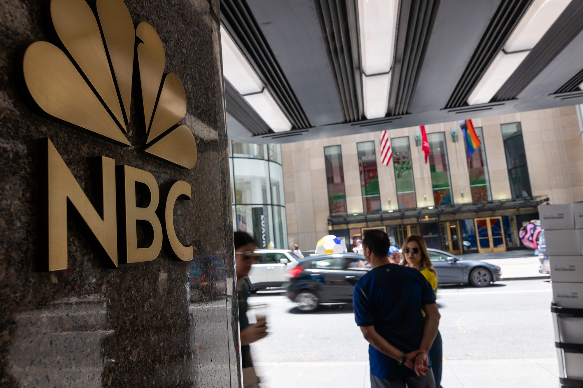 People walk by the NBC logo in Rockefeller Center.