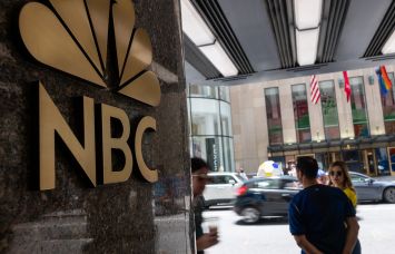 People walk by the NBC logo in Rockefeller Center.