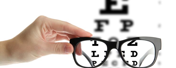 A photo illustration of reading eyeglasses in a hand in front of an eye chart.