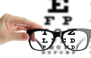 A photo illustration of reading eyeglasses in a hand in front of an eye chart.