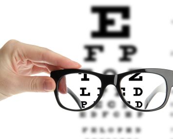 A photo illustration of reading eyeglasses in a hand in front of an eye chart.