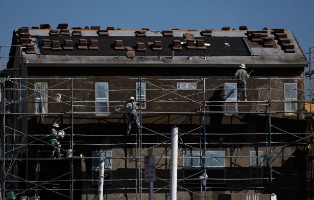 Construction workers stand on scaffolding as they work on a home under construction.