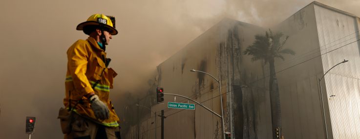 A firefighter walks down the street as a massive warehouse fire at a Lineage cold storage facility burns on June 20 in Los Angeles.