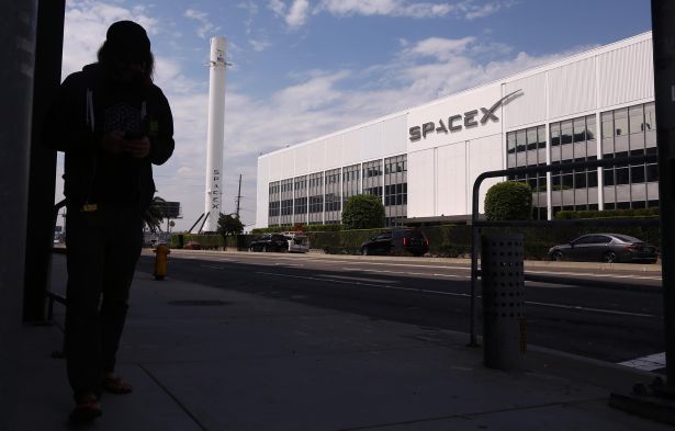 A SpaceX employee waits to cross the street from employee parking to SpaceX in Hawthorne, Calif.
