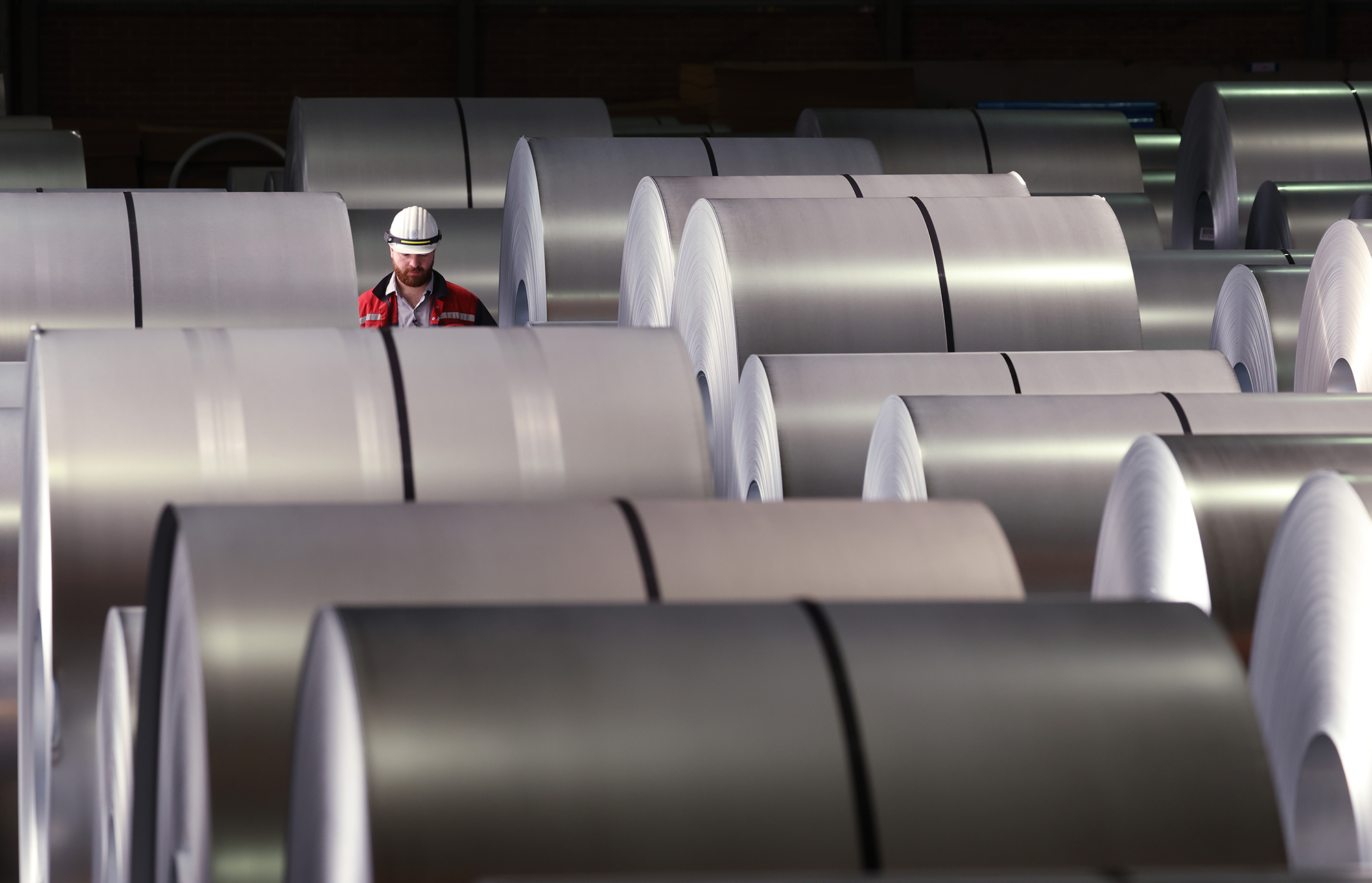 A worker walks among coils of finished steel at the Thyssenkrupp steel plant in Duisburg, Germany.