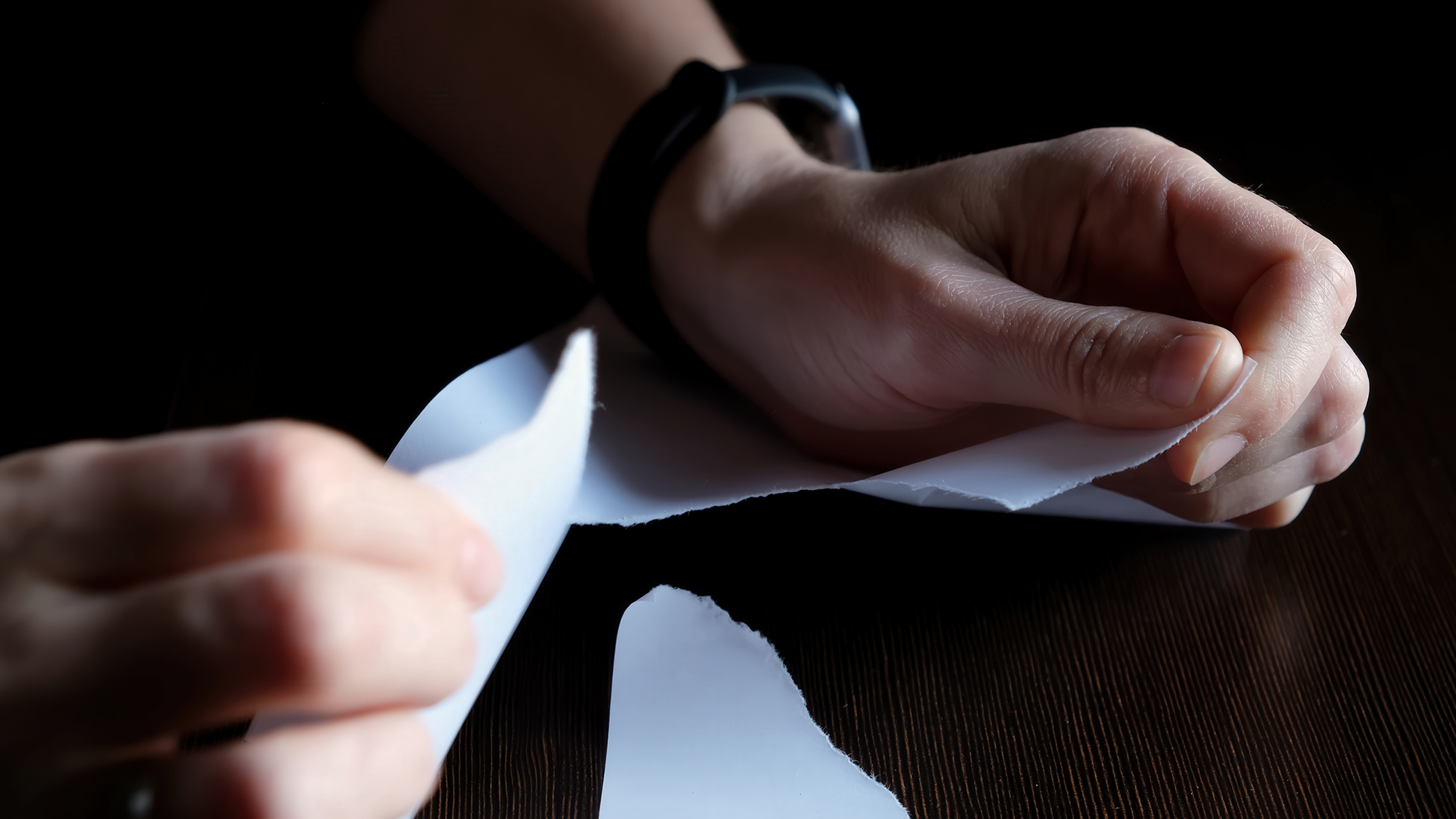 A pair of hands tearing up a piece of paper.