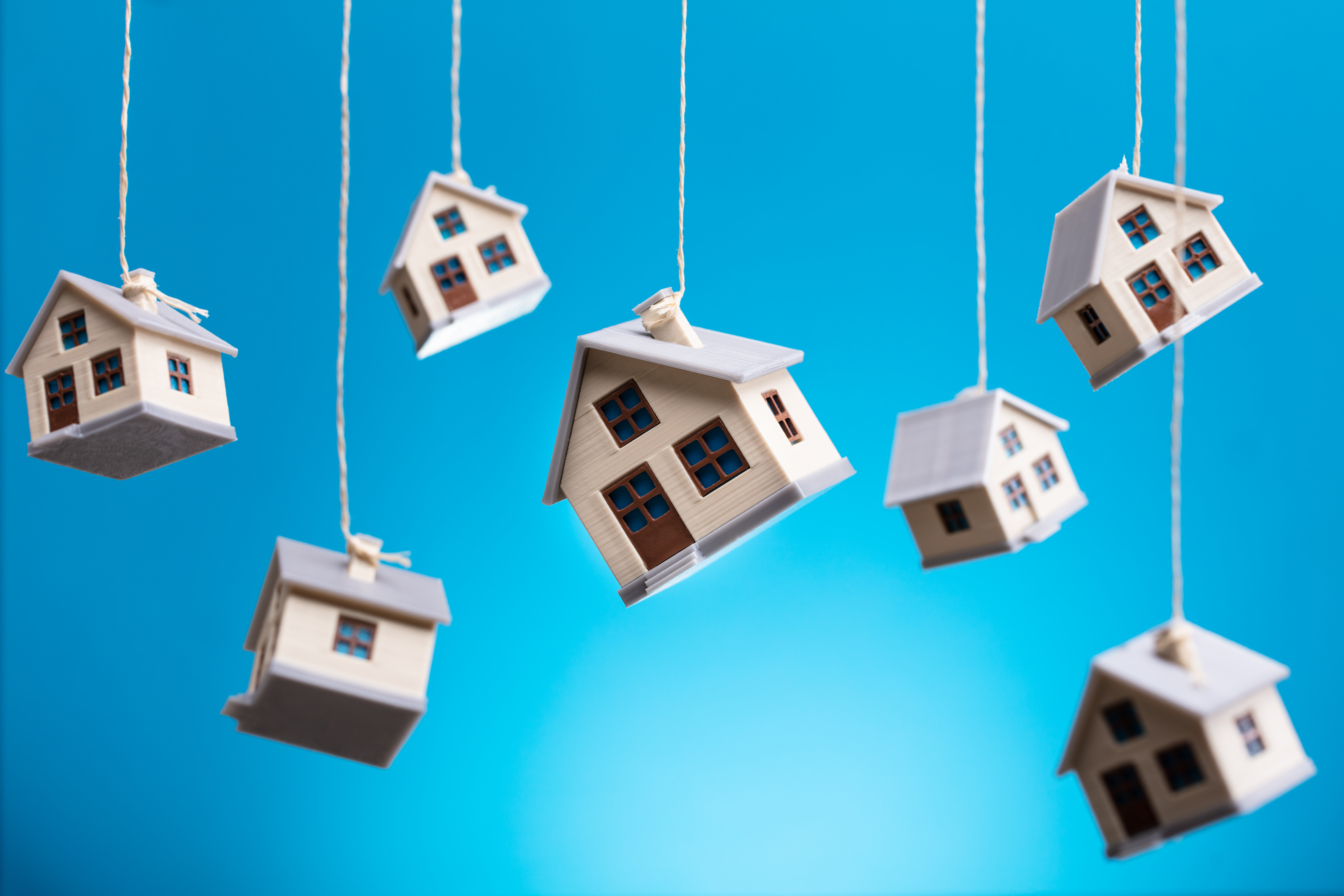 Miniature Houses Hanging By Strings Against Blue.