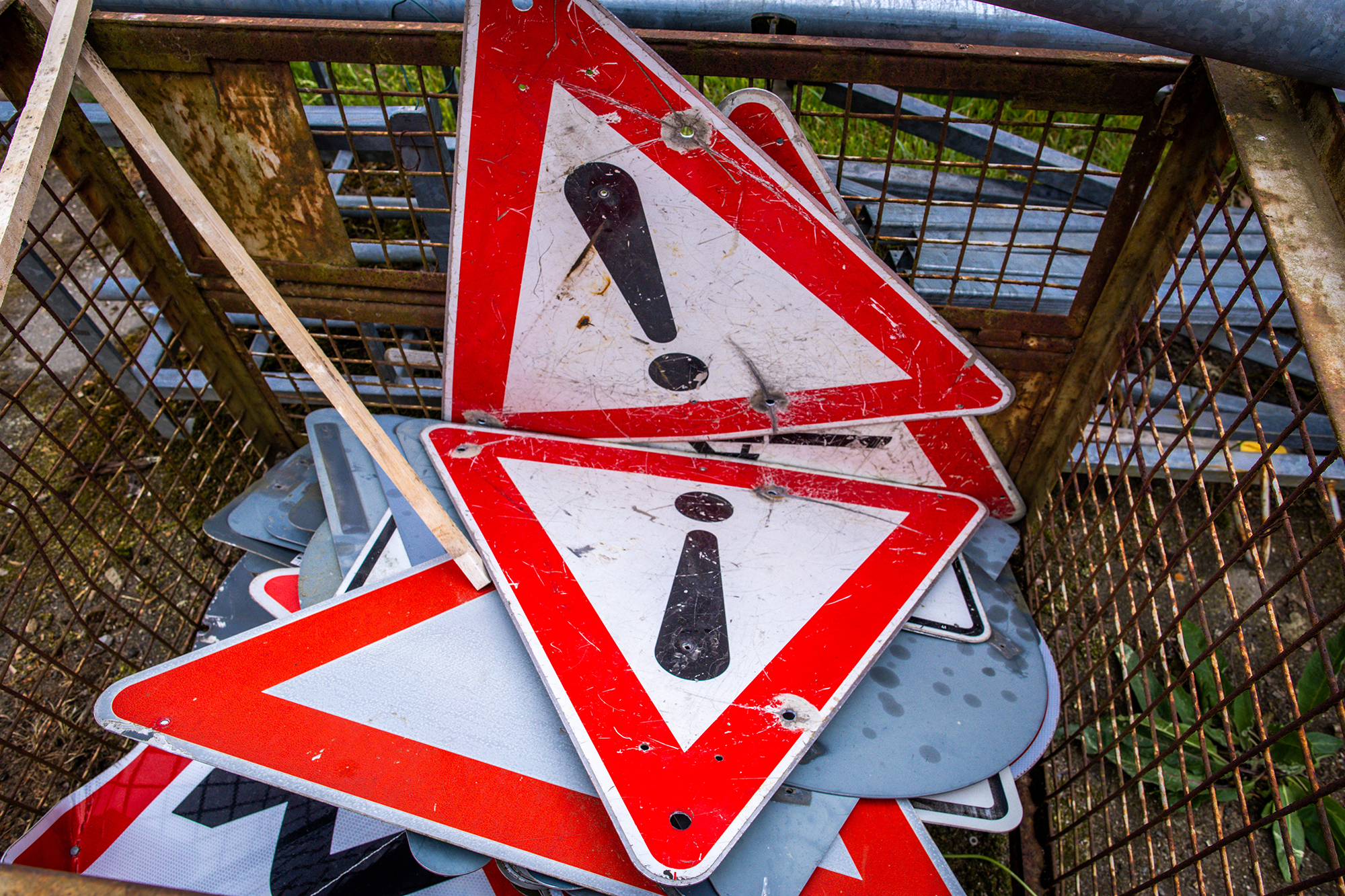 Worn-out and dented traffic signs lie in a collection container.