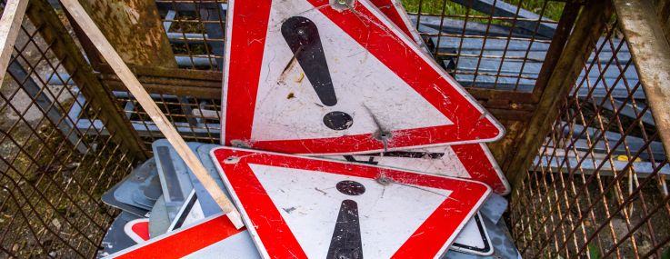 Worn-out and dented traffic signs lie in a collection container.