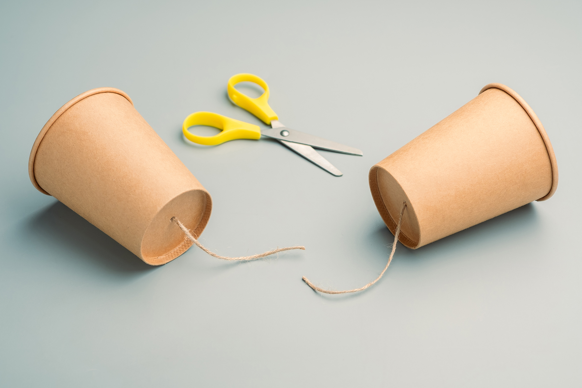 Two paper cups formerly connected by a cut piece of string with a pair of scissors nearby.
