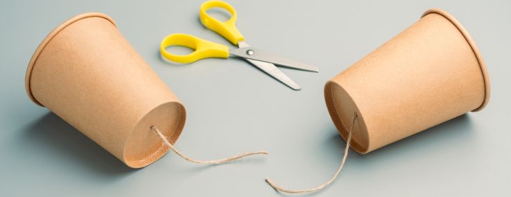 Two paper cups formerly connected by a cut piece of string with a pair of scissors nearby.