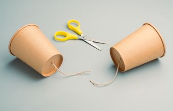 Two paper cups formerly connected by a cut piece of string with a pair of scissors nearby.