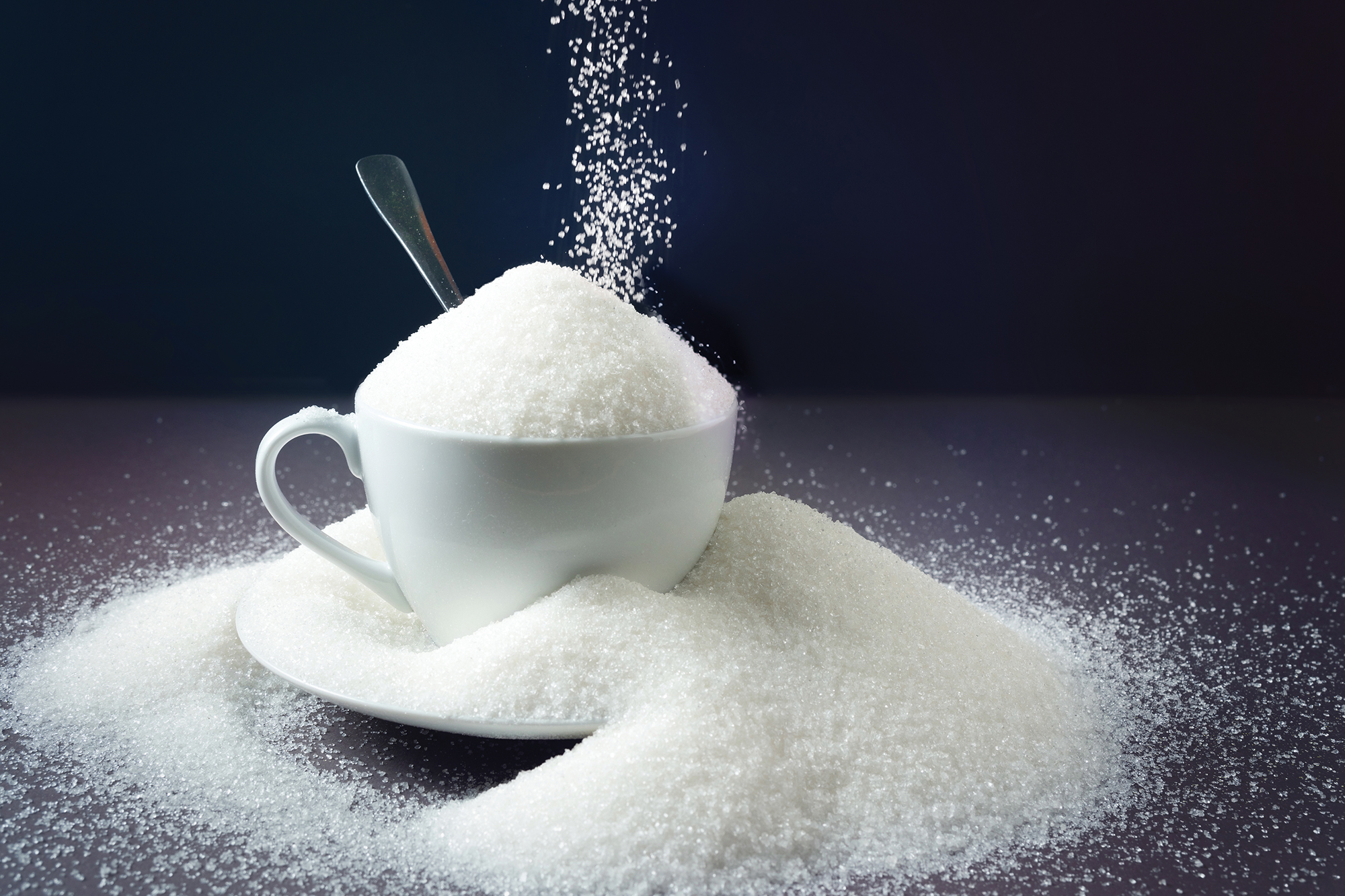 Sugar being poured into an overflowing cup filled with sugar.