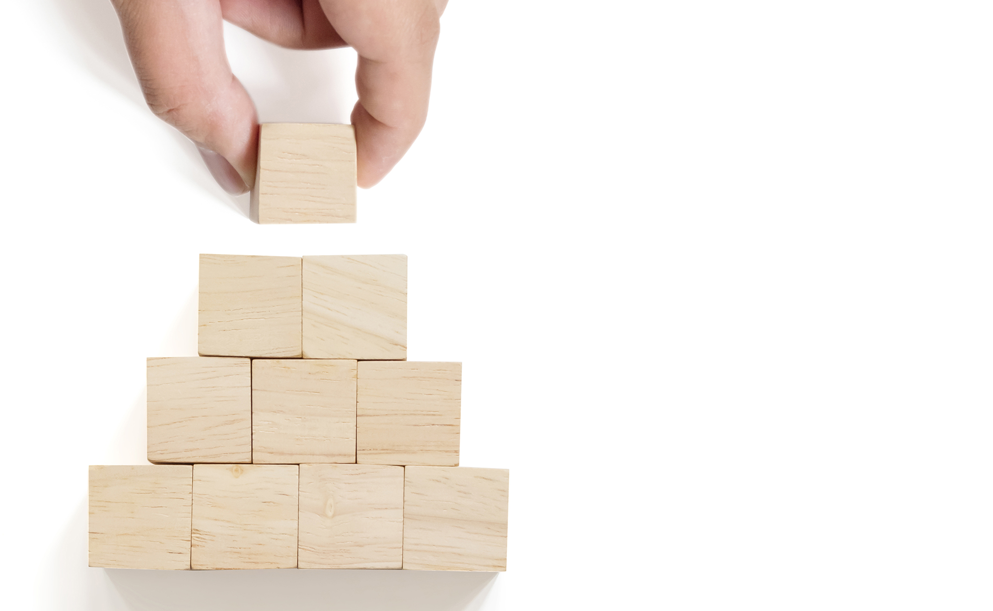 Hand arranging wood block stacking on top pyramid with white background. Business concept for growth success process